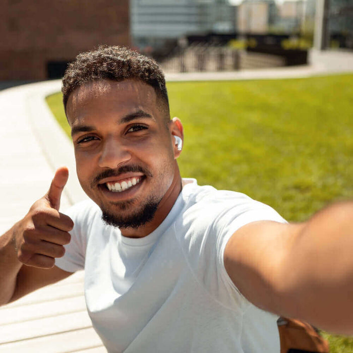 Junger Mann macht ein Selfie im Freien, trägt Kopfhörer und zeigt Daumen hoch, gute Stimmung.