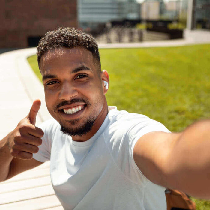 Junger Mann macht ein Selfie im Freien, trägt Kopfhörer und zeigt Daumen hoch, gute Stimmung.