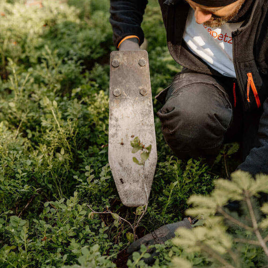 Ein Gärtner benutzt eine spezielle Schaufel, um Pflanzen im grünen Garten zu bearbeiten und zu pflanzen.