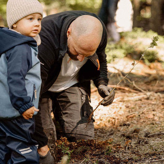 Ein Erwachsener pflanzt einen Baum mit einem Kind im Wald, umgeben von Natur.