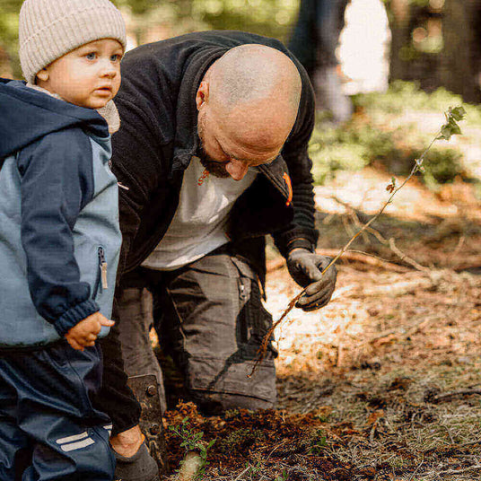Ein Erwachsener pflanzt einen Baum mit einem Kind im Wald, umgeben von Natur.