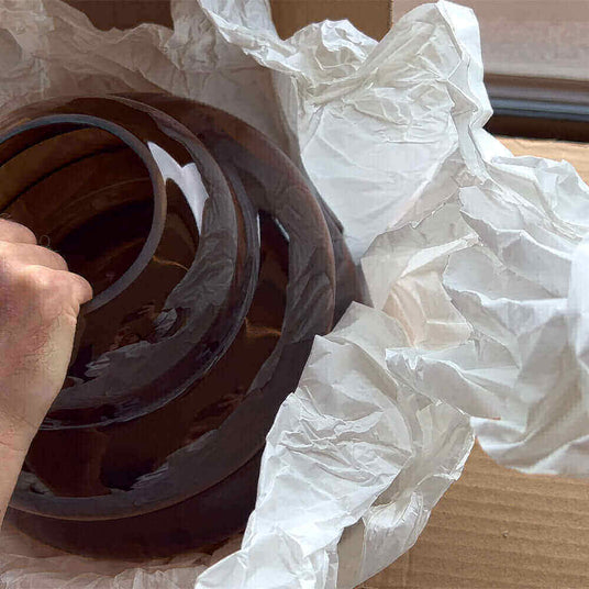 Hand entnimmt braune dekorative Schalen aus einer Kartonverpackung mit Papier.