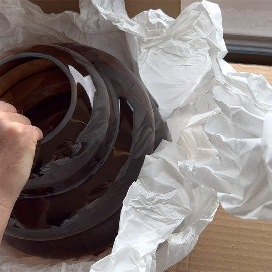 Hand entnimmt braune dekorative Schalen aus einer Kartonverpackung mit Papier.