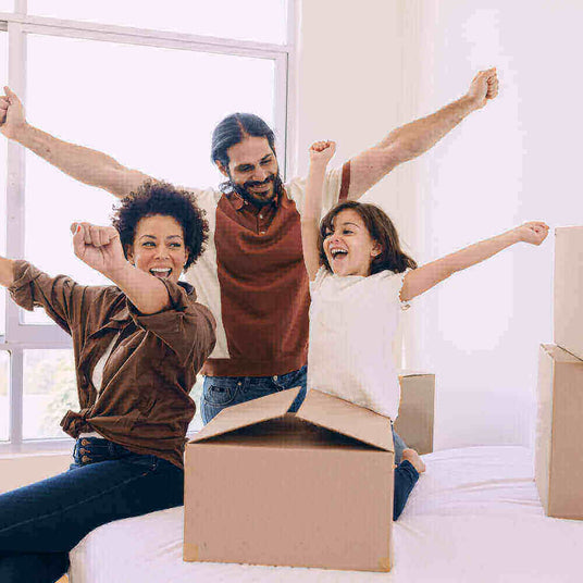 Eine fröhliche Familie mit einem Kind, das in einem neuen Zuhause zusammen feiert, mit Umzugskartons um sie herum.