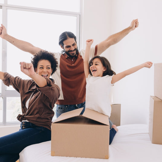 Eine fröhliche Familie mit einem Kind, das in einem neuen Zuhause zusammen feiert, mit Umzugskartons um sie herum.