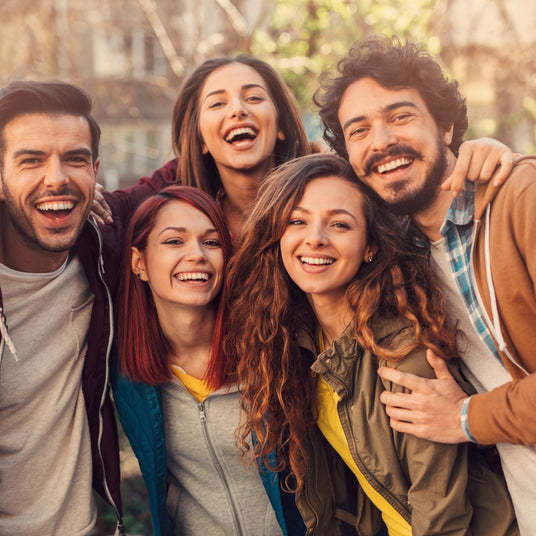 Eine Gruppe fröhlicher junger Menschen lächelt gemeinsam in einem sonnigen Park.