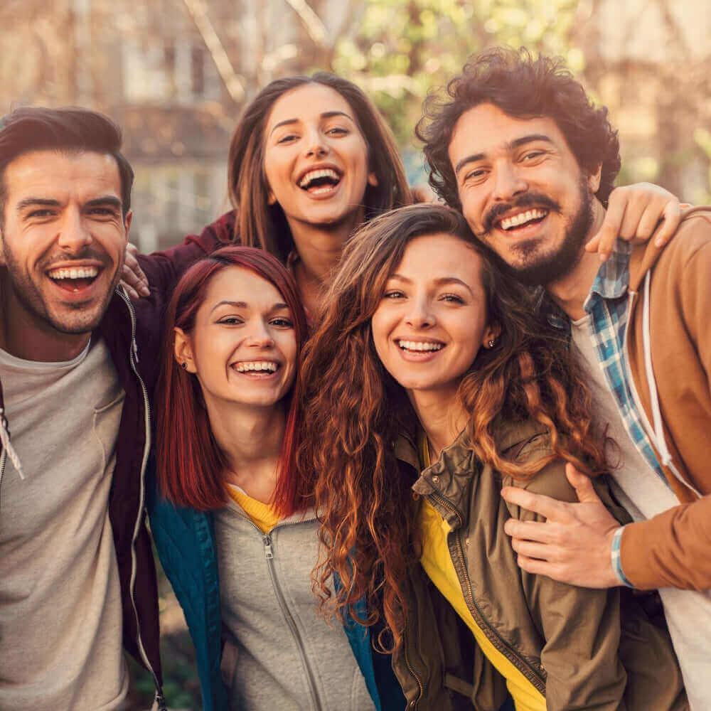 Eine Gruppe fröhlicher junger Menschen lächelt gemeinsam in einem sonnigen Park.