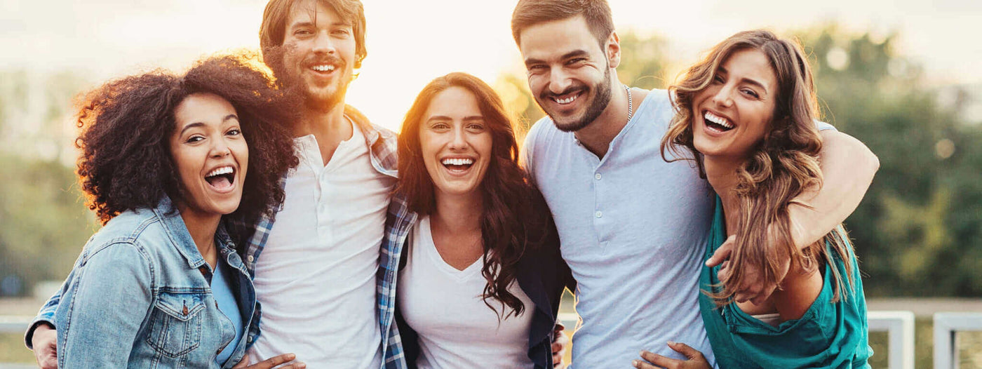 Fünf fröhliche Freunde umarmen sich im Freien, lächeln und genießen einen sonnigen Tag zusammen.