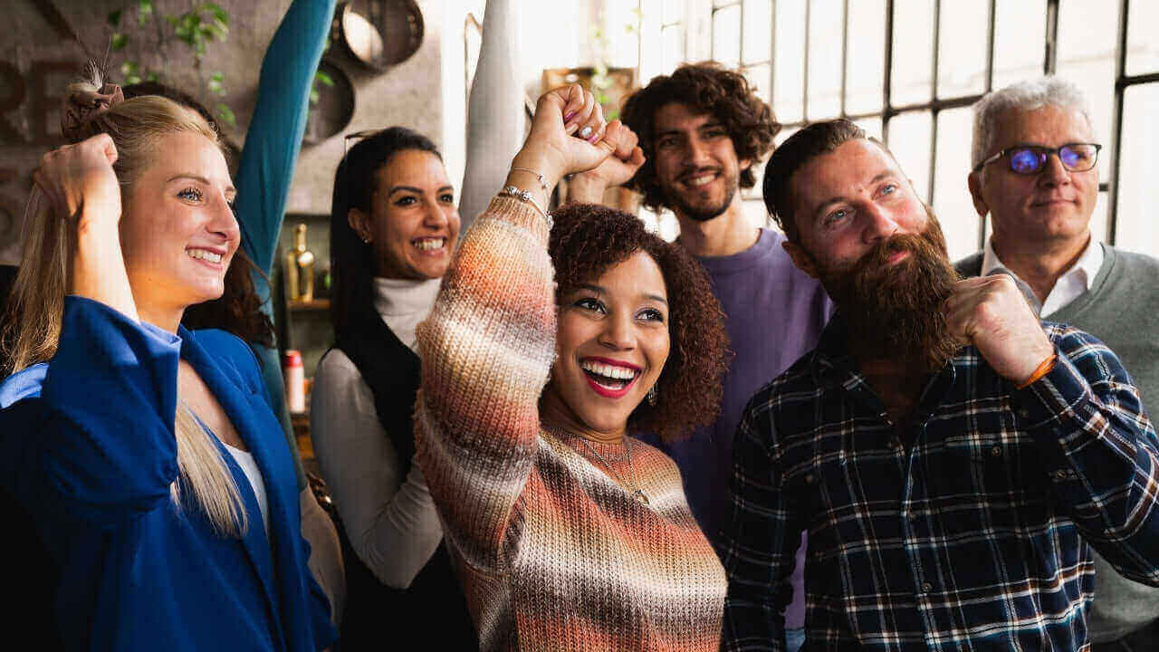 Junge Menschen feiern zusammen in einem modernen Raum, lächelnd und begeistert, positive Energie und Teamgeist ausstrahlend.