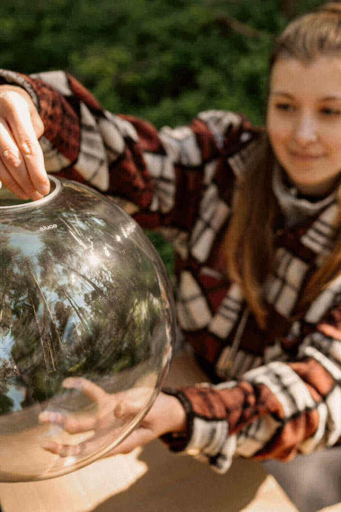 Ein Mädchen hält eine große Glaskugel in der Natur, lächelt und genießt den Moment.