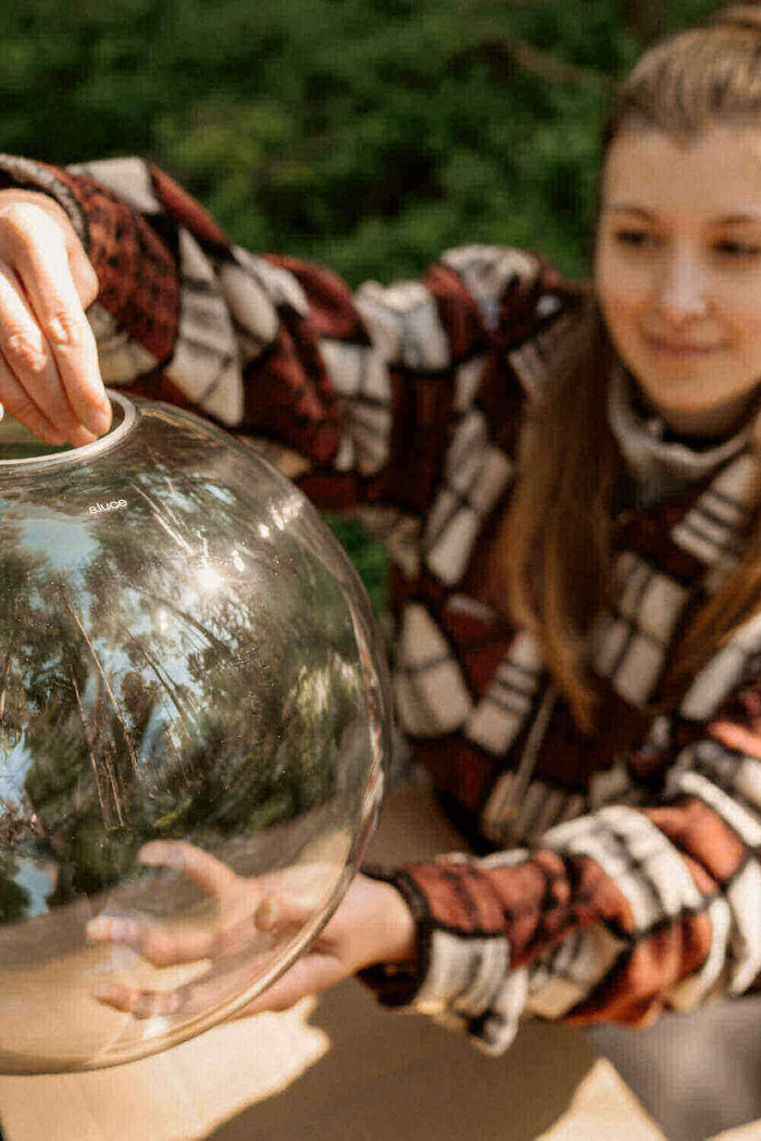 Ein Mädchen hält eine große Glaskugel in der Natur, lächelt und genießt den Moment.