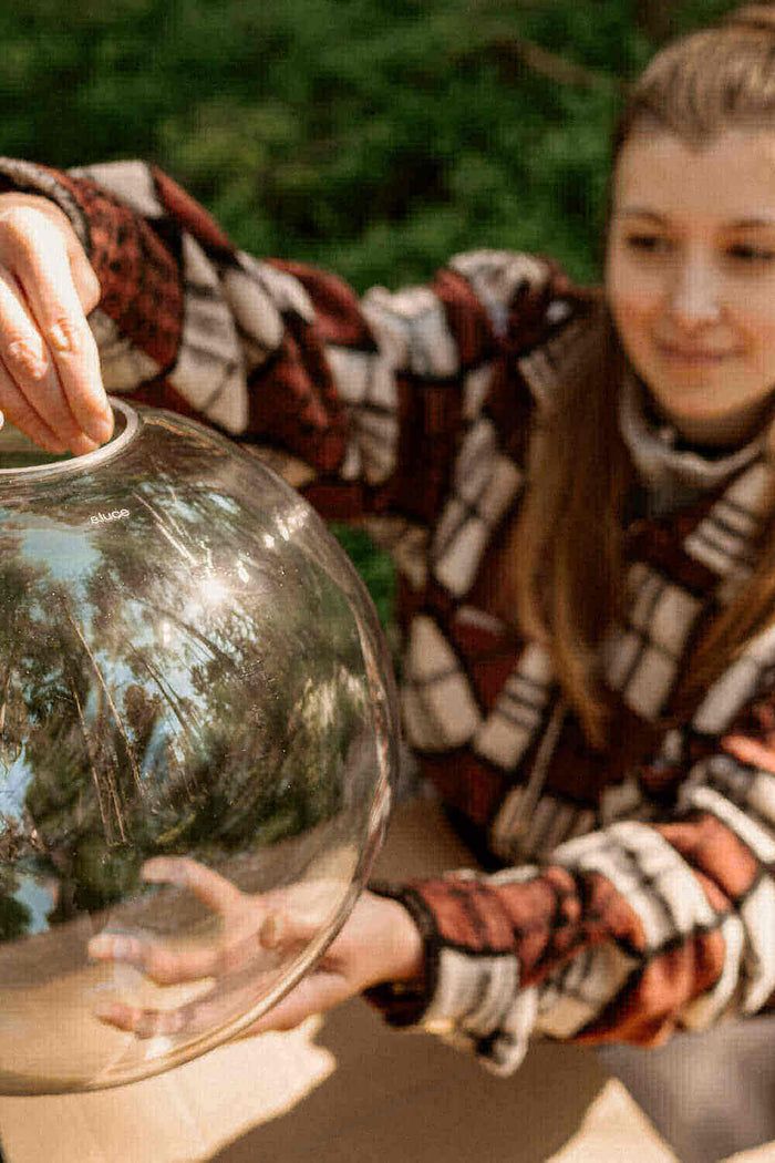 Ein Mädchen hält eine große Glaskugel in der Natur, lächelt und genießt den Moment.
