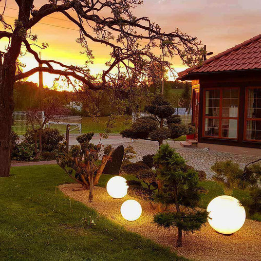 Schöne Gartenansicht bei Sonnenuntergang mit leuchtenden Kugellampen und angrenzender Terrasse.