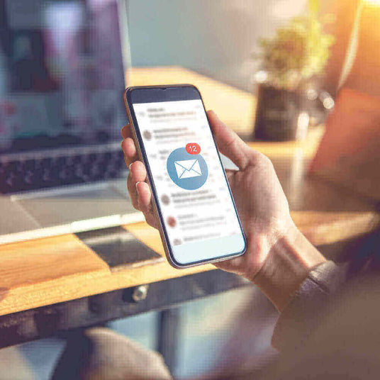 Person nutzt Smartphone mit E-Mail-Benachrichtigung, 12 neue Nachrichten, im modernen Arbeitsumfeld.