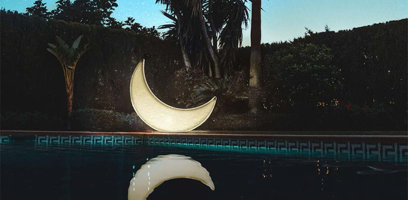 Beleuchteter Halbmond neben einem Pool, umgeben von Pflanzen und nachts unter dem Sternenhimmel.