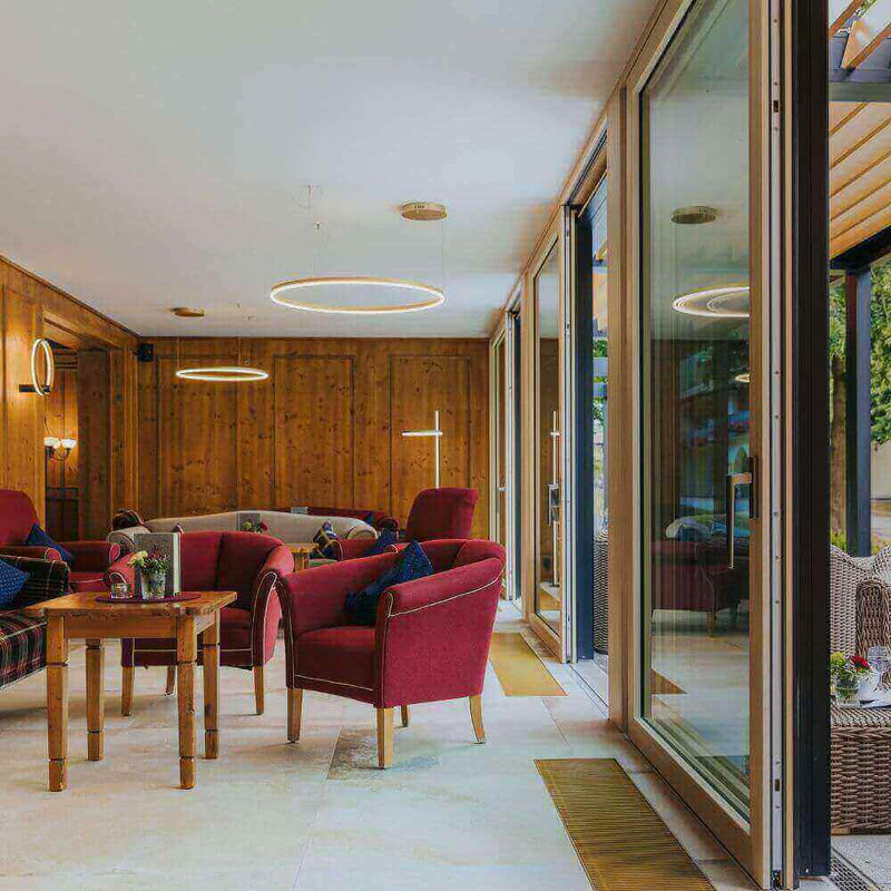 Gemütliches Wohnzimmer mit roten Sesseln und großen Fenstern, moderne Beleuchtung im Holzinterieur.