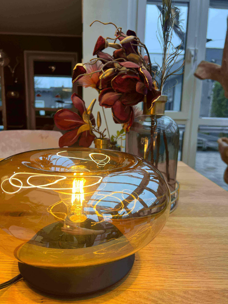 Stimmungsvolle Tischlampe mit warmem Licht und eleganten Trockenblumen im Hintergrund, gemütliches Ambiente.