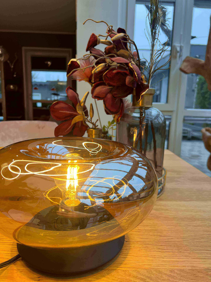 Stimmungsvolle Tischlampe mit warmem Licht und eleganten Trockenblumen im Hintergrund, gemütliches Ambiente.