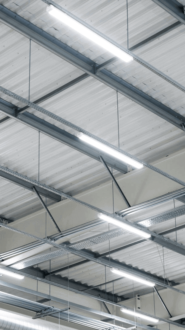 Moderne Industriebeleuchtung im Deckenbereich eines großen Raums mit Metallträgern und Leuchten.