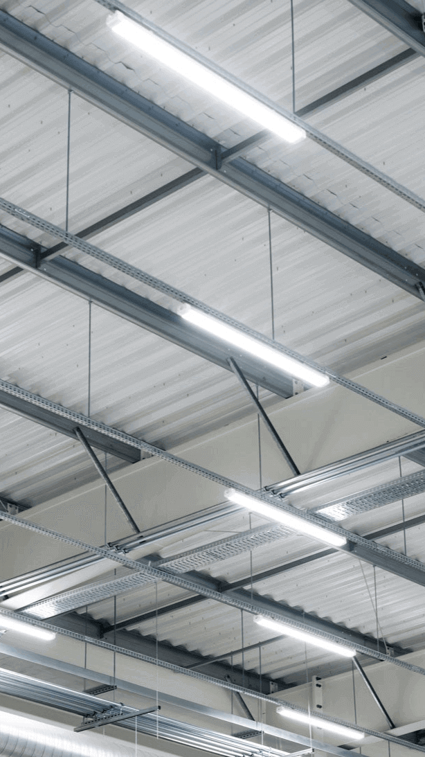 Moderne Industriebeleuchtung im Deckenbereich eines großen Raums mit Metallträgern und Leuchten.