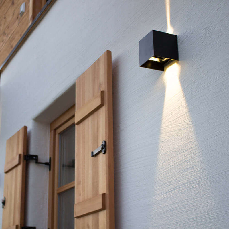 Moderne Wandleuchte an hellem Außenbereich mit Holzfensterläden beleuchtet den Raum.