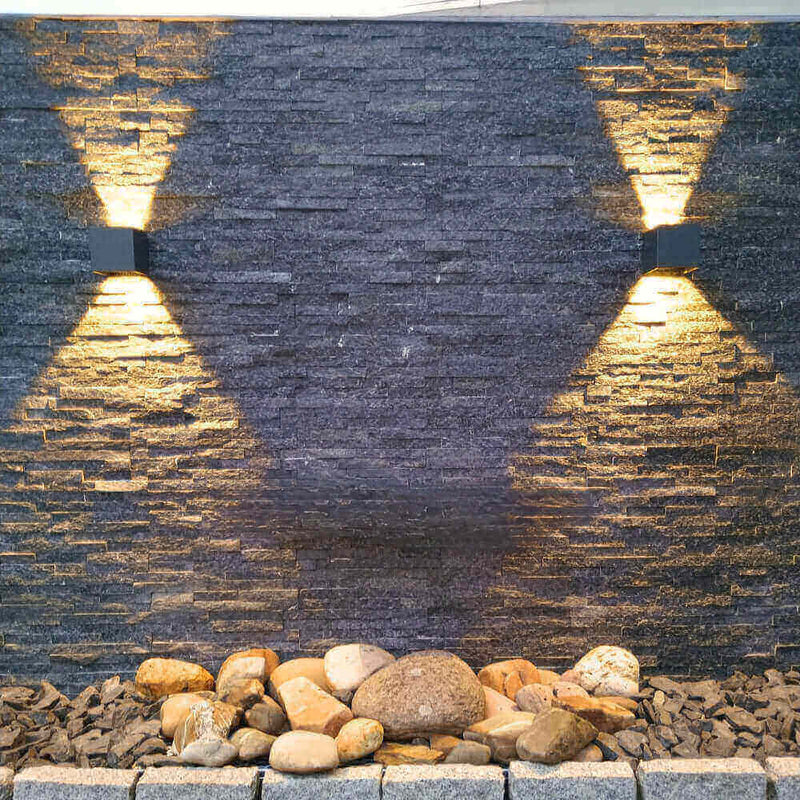 Moderne Wandbeleuchtung an einer Steinwand mit Steinen im Vordergrund, stilvoll und elegant.