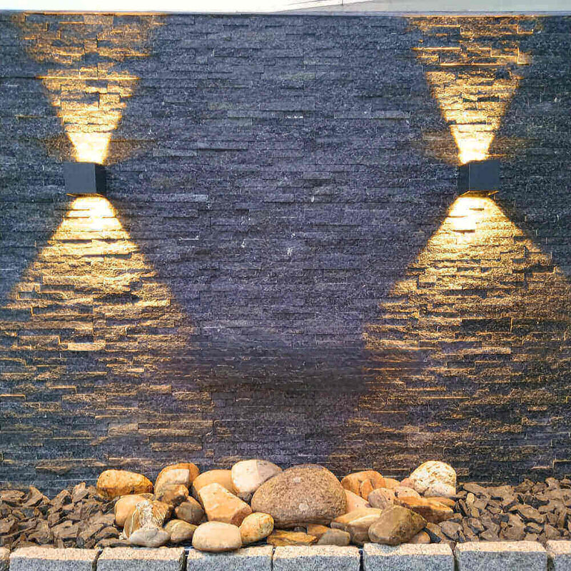Moderne Wandbeleuchtung an einer Steinwand mit Steinen im Vordergrund, stilvoll und elegant.