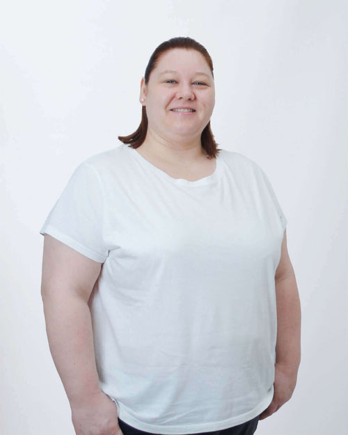 Frau in weißem T-Shirt vor neutralem Hintergrund, freundliches Lächeln, selbstbewusste Pose.