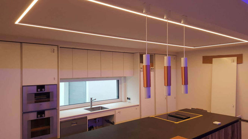 Moderne Küche mit LED-Deckenbeleuchtung und eleganten Pendellichtern über einer Kücheninsel.