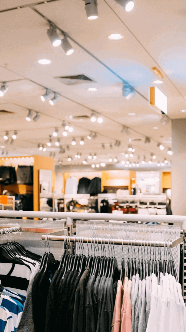 Beleuchtung und Kleidung in einem modernen Bekleidungsgeschäft, mit Regalen und ansprechendem Layout.