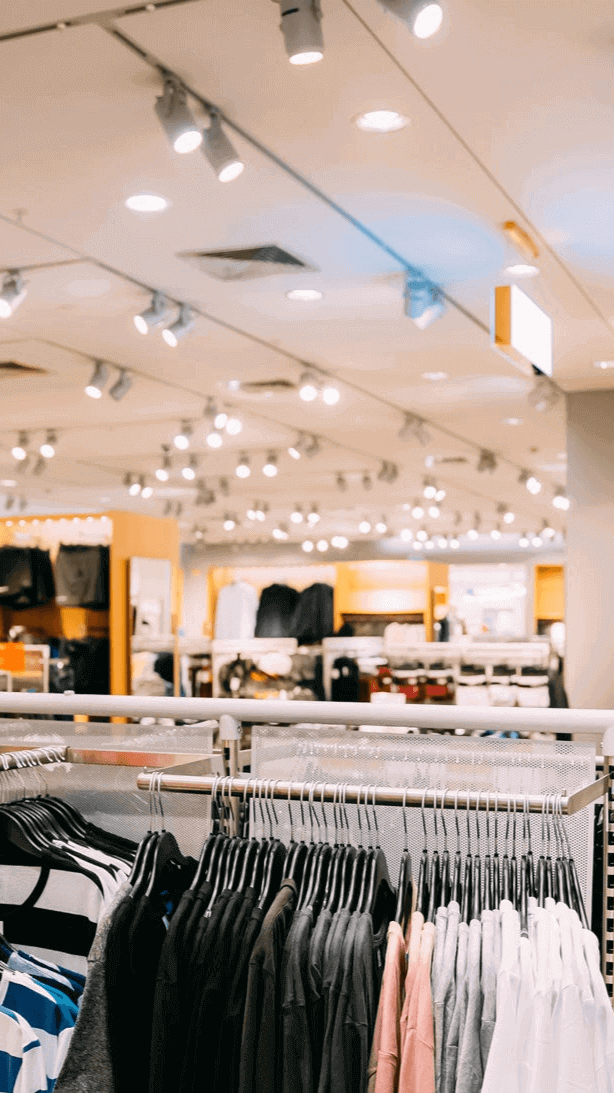 Beleuchtung und Kleidung in einem modernen Bekleidungsgeschäft, mit Regalen und ansprechendem Layout.