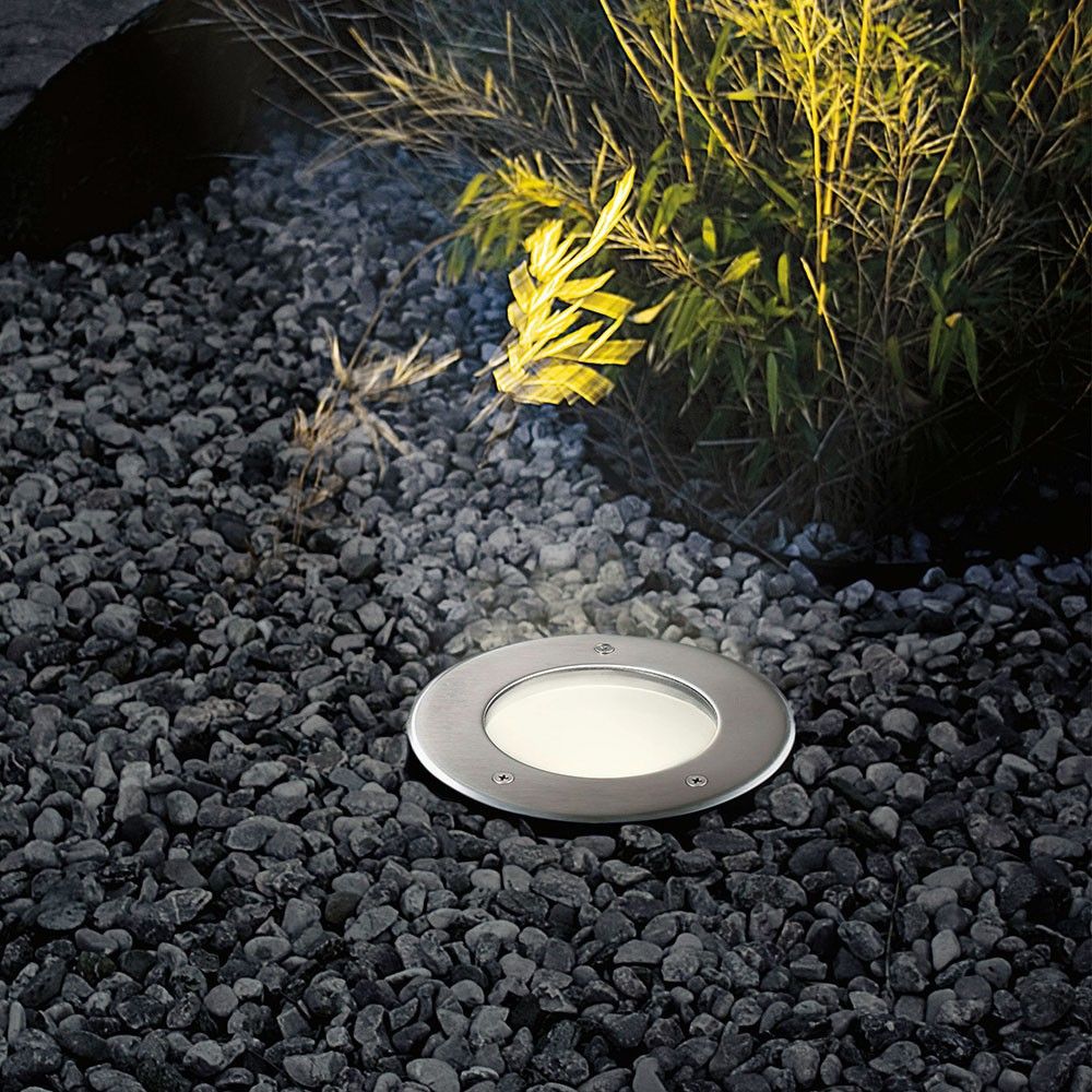 Runder Edelstahl Bodeneinbaustrahler IP67 im Garten, eingebaut in Kiesbett mit Leuchteffekten.