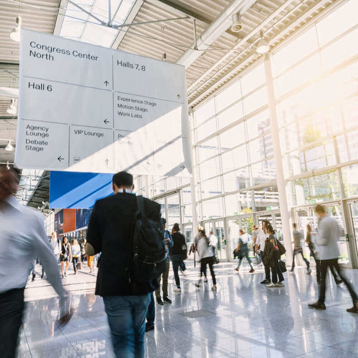 Menschen im Congress Center mit Richtungsschildern zu Hallen und Lounges, Lichtdurchflutet, geschäftige Atmosphäre.
