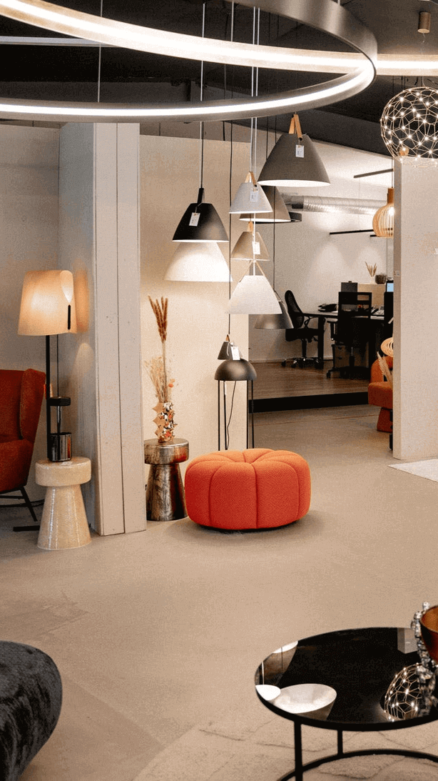 Modernes Möbelgeschäft mit stilvollen Lampen, einem roten Pouf und eleganten Möbeln im Hintergrund.