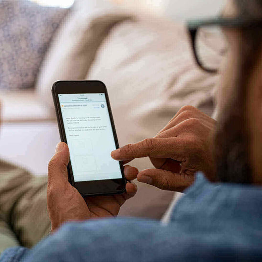 Person nutzt ein Smartphone und tippt auf dem Bildschirm, während er entspannt auf einem Sofa sitzt.