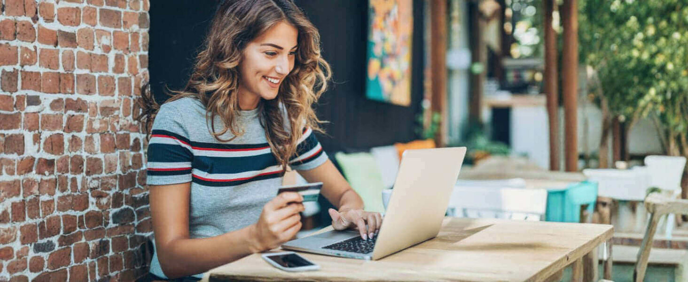 Junge Frau mit Kreditkarte am Laptop in einem Café, lächelnd und online einkaufend.