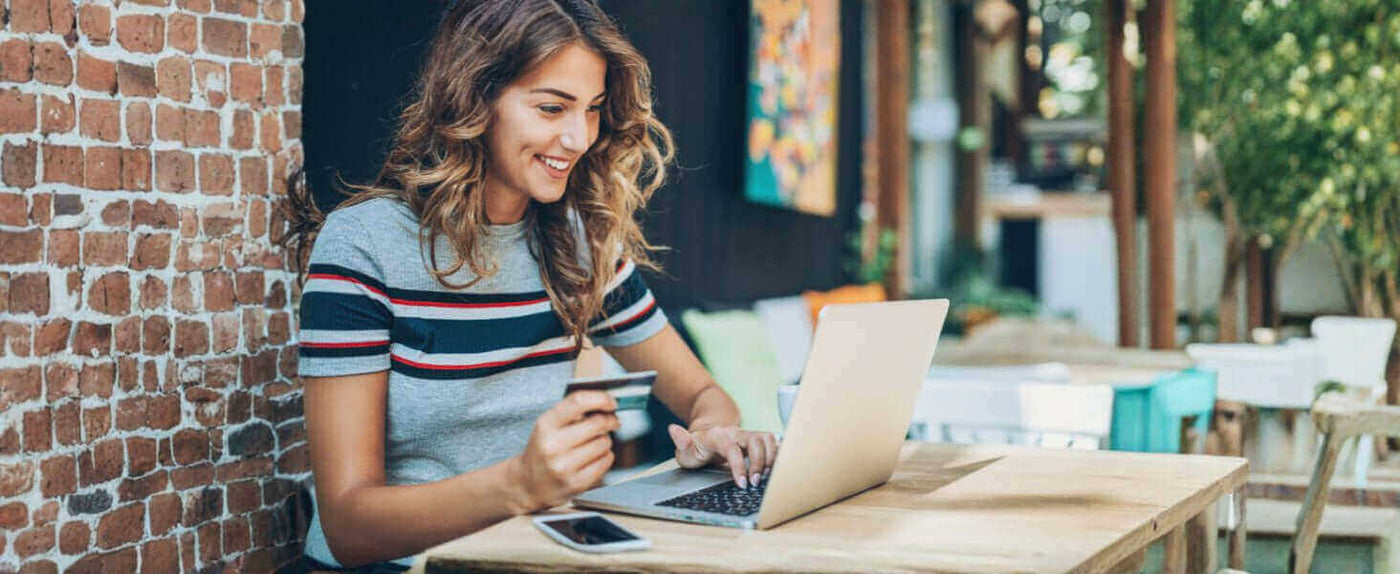 Junge Frau mit Kreditkarte am Laptop in einem Café, lächelnd und online einkaufend.