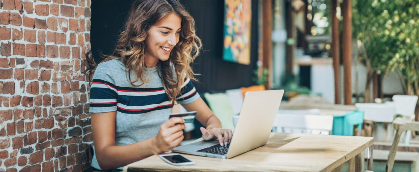 Junge Frau mit Kreditkarte am Laptop in einem Café, lächelnd und online einkaufend.