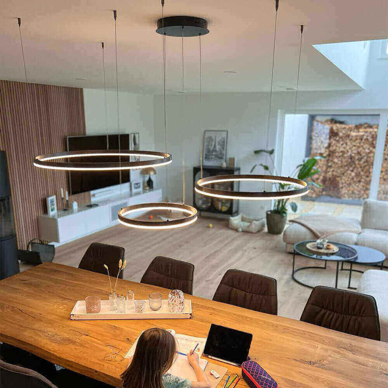 Moderne s.luce Pendelleuchte über einem Holztisch in einem lichtdurchfluteten Wohnraum.