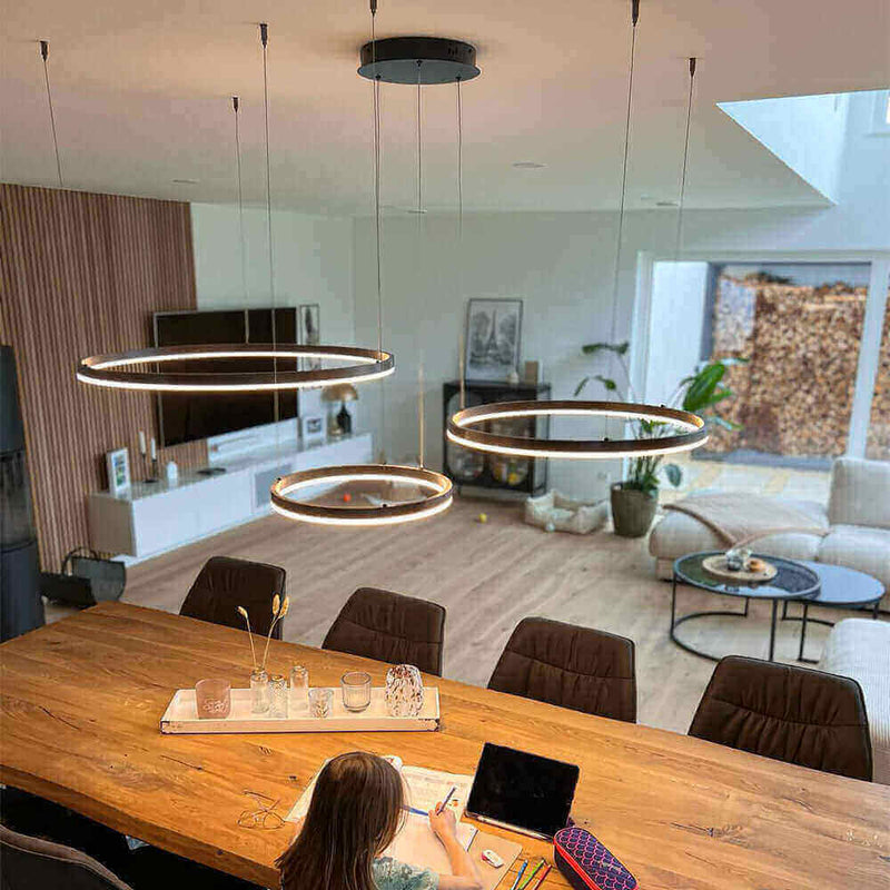 Moderne s.luce Pendelleuchte über einem Holztisch in einem lichtdurchfluteten Wohnraum.