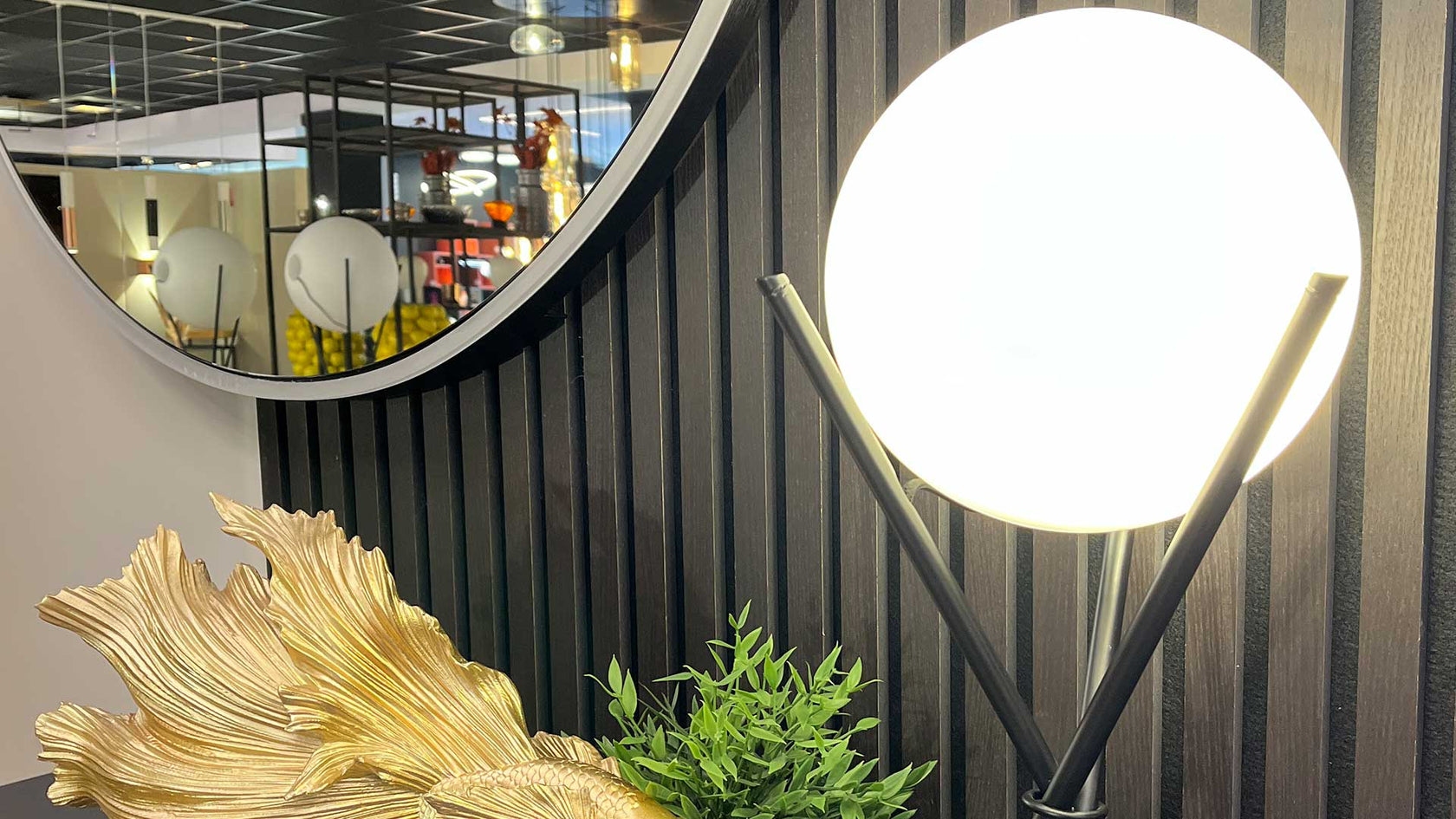 Wandleuchte mit rundem Lampenschirm, goldener Pflanze und Spiegel im modernen Innenraum.