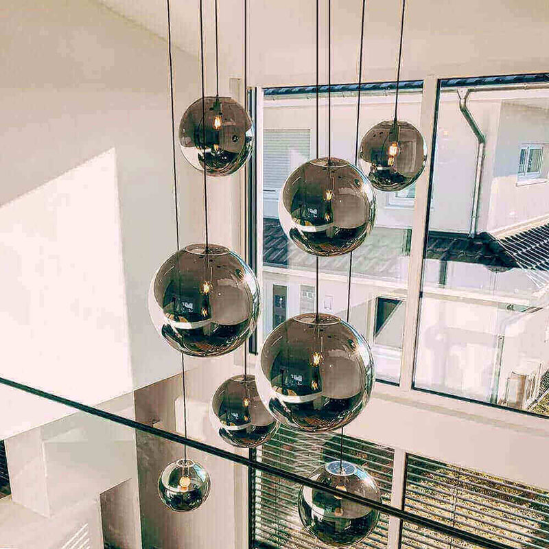 Moderne Pendelleuchten in runden, reflektierenden Kugeln, hängen an dünnen Kabeln in einem hellen Raum.