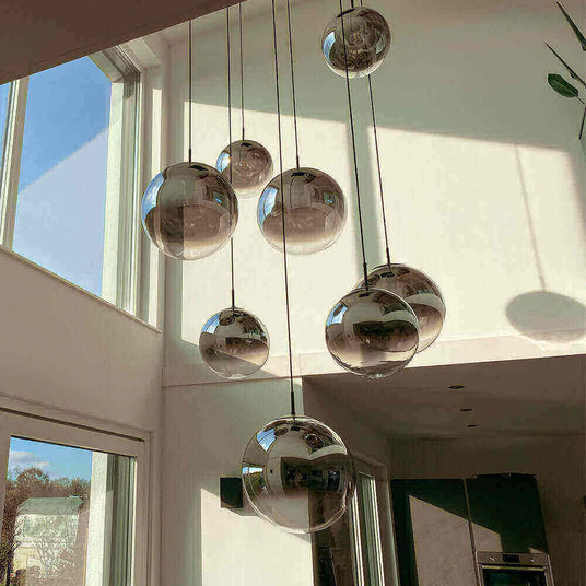 Moderne Pendelleuchten in einem hellen Raum mit großen Spiegelkugeln, die das Licht reflektieren.