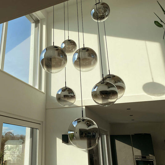 Moderne Pendelleuchten in einem hellen Raum mit großen Spiegelkugeln, die das Licht reflektieren.