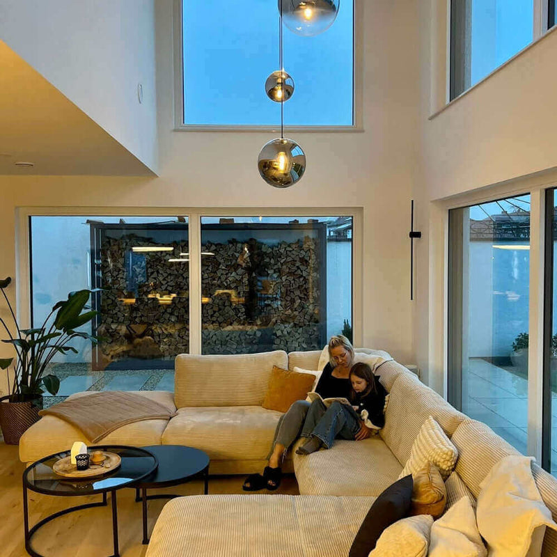 Gemütliches Wohnzimmer mit modernen Fenstern, einer Couch und einer Mutter mit Kind beim Lesen.