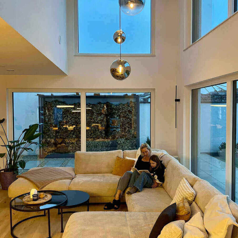 Gemütliches Wohnzimmer mit modernen Fenstern, einer Couch und einer Mutter mit Kind beim Lesen.