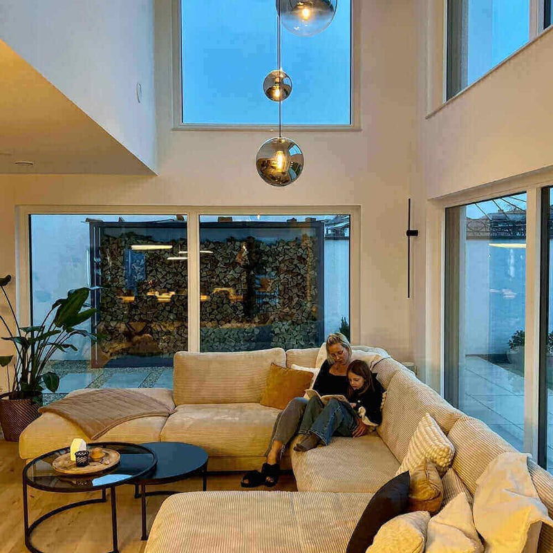 Gemütliches Wohnzimmer mit modernen Fenstern, einer Couch und einer Mutter mit Kind beim Lesen.