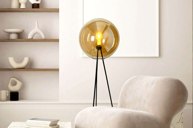 Moderne Stehlampe mit goldener Glaskugel in stilvollem Wohnraum mit gemütlicher Couch.
