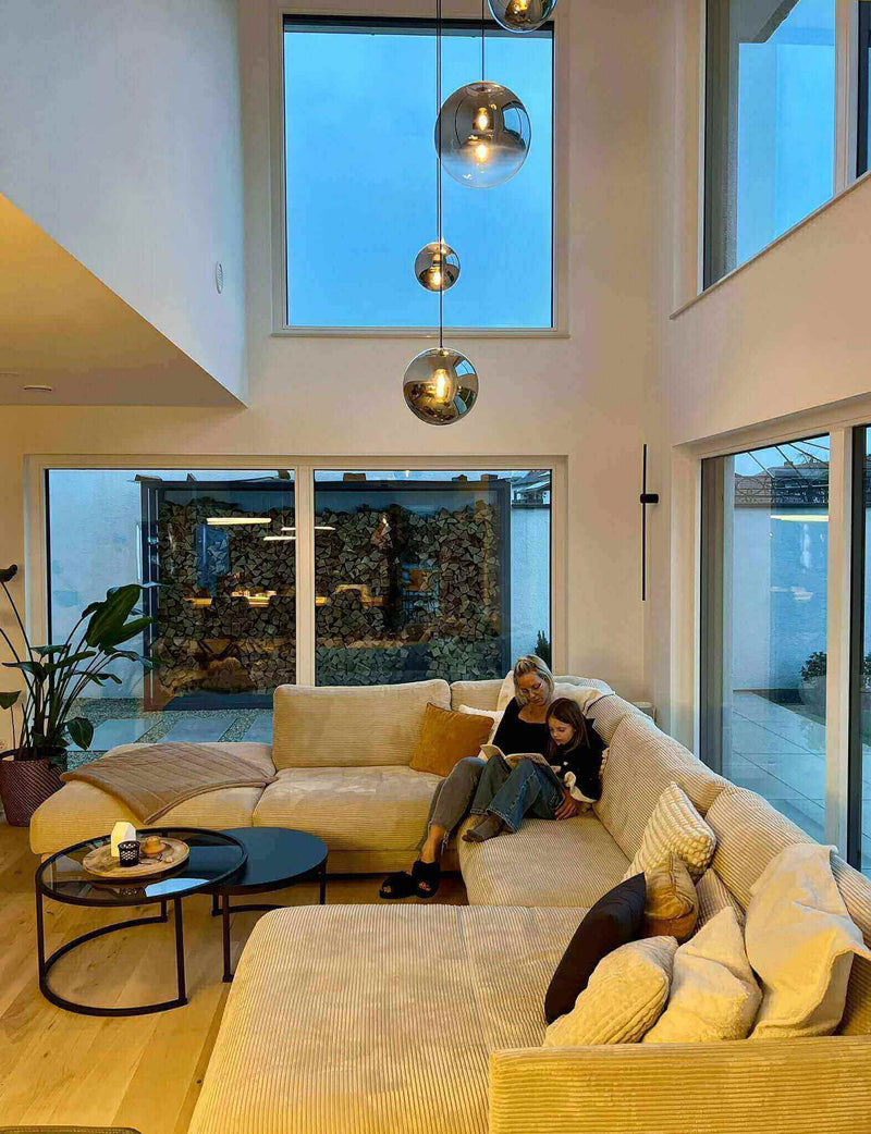 Gemütliches Wohnzimmer mit großem Sofa, Mutter mit Kind beim Lesen, große Fenster, moderne Einrichtung.
