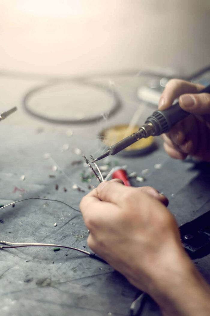 Hände beim Löten von Drähten an einem Werkstatttisch mit Werkzeugen
